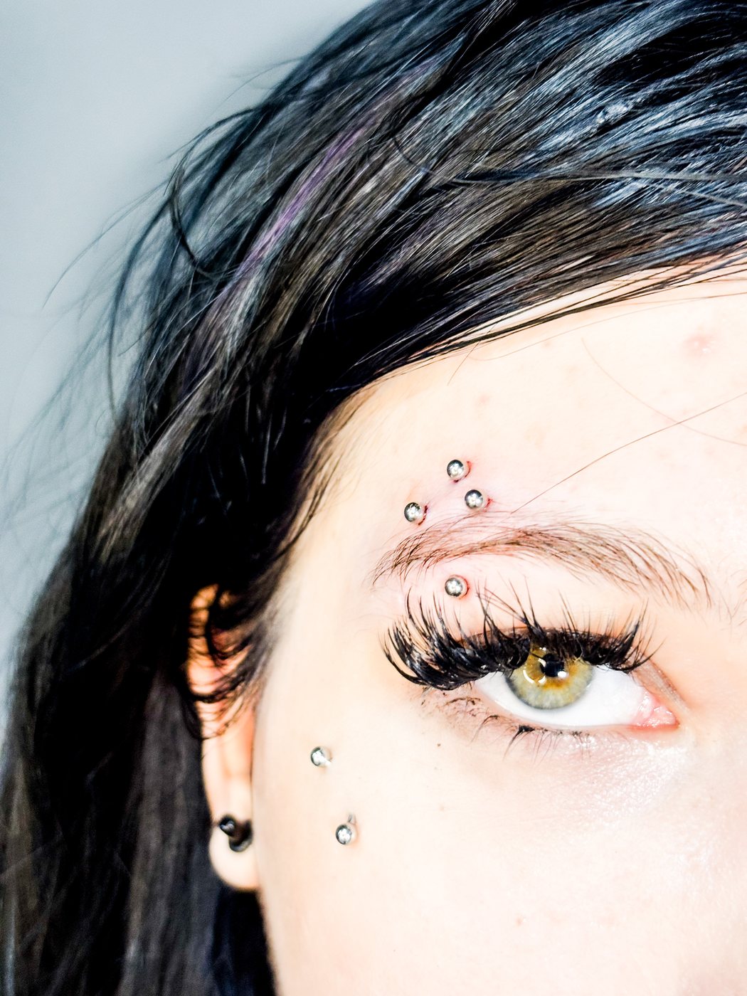 cross eyebrow piercing with surface studs under the eye