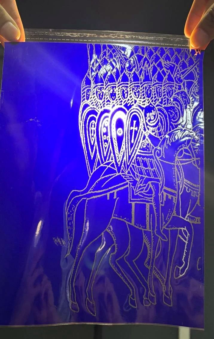 hectograph stencil held up to the light: silver line drawing of armoured riders on a deep blue transfer sheet